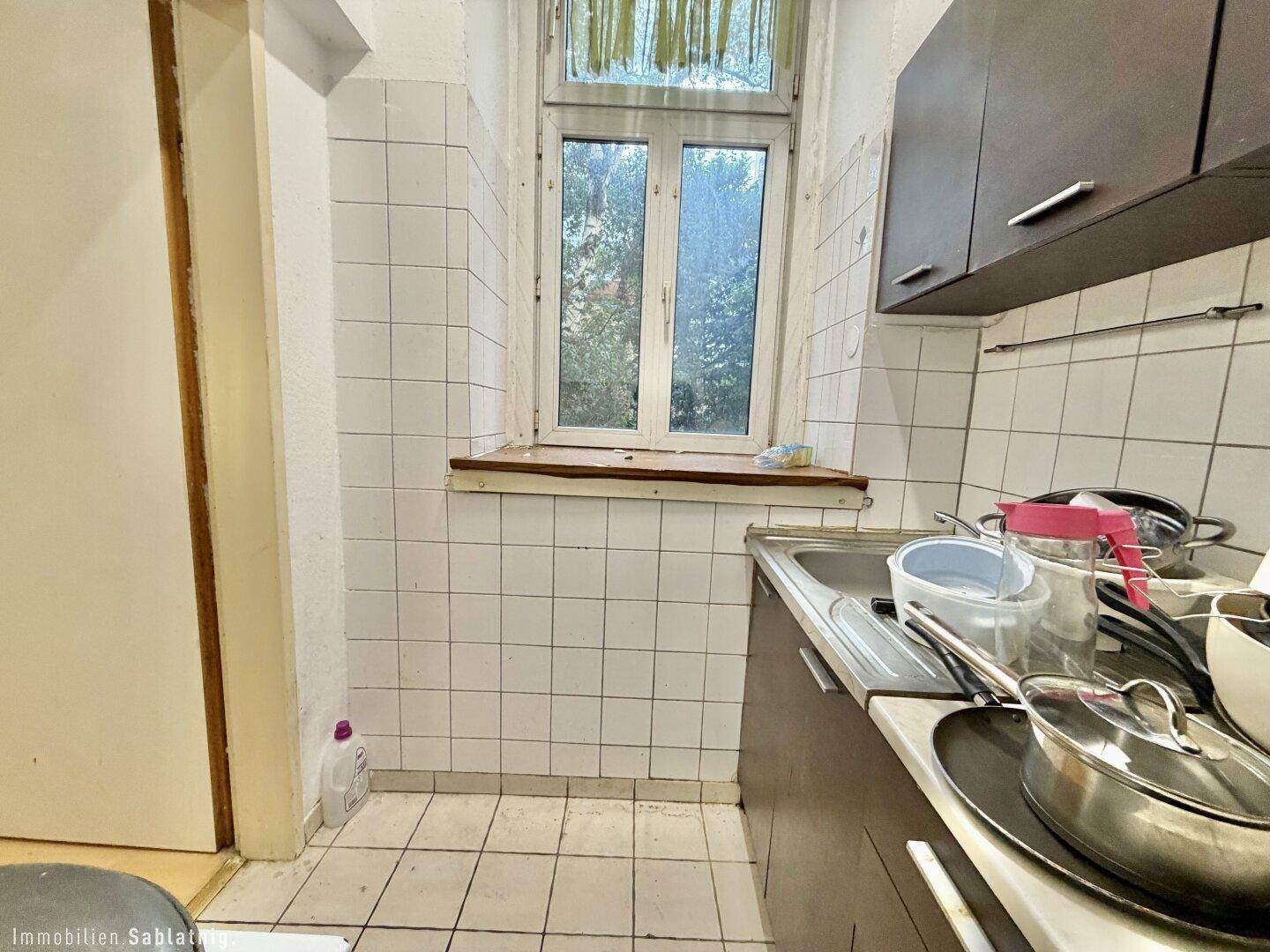 Kleine Küche mit Spüle, Oberschränken und einem Fenster.