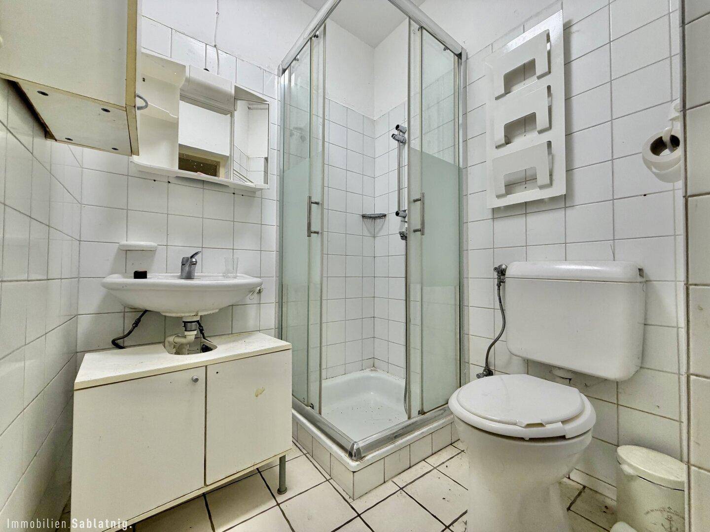 Badezimmer mit Dusche, WC, Waschbecken und weißen Fliesen.