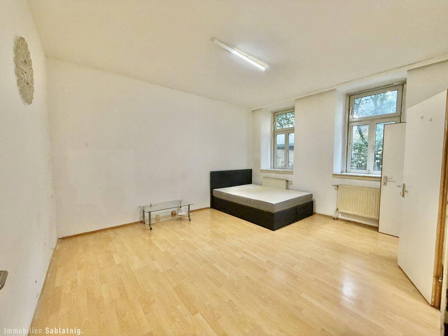 Geräumiges Schlafzimmer mit Holzboden, zwei Fenstern und viel Tageslicht.