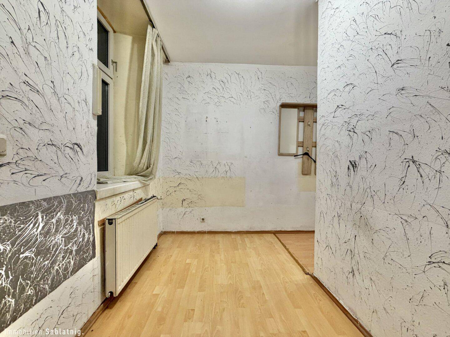 Heller Wohnraum mit strukturierten Wänden, Fenster und Heizkörper.