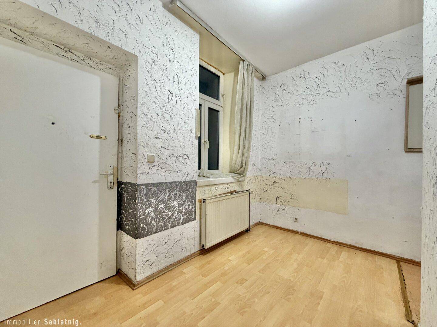 Zimmer mit Fenster, Heizkörper und einer Tür, die in den Raum führt.