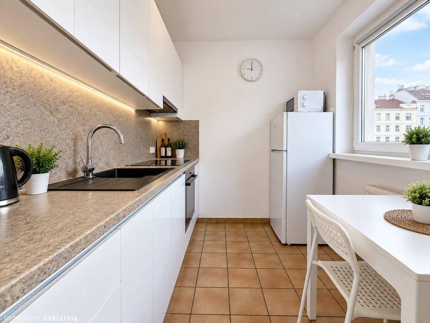 Funktionale Küche mit weißen Schränken, Fliesenboden und Fenster mit Stadtblick.