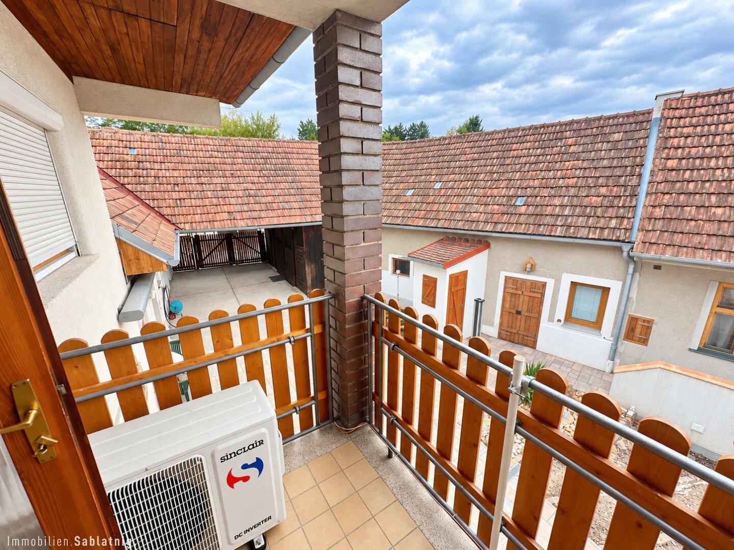 Kleiner Balkon mit Holzzaun und Klimaanlage-Außengerät, Blick auf Nachbargebäude.