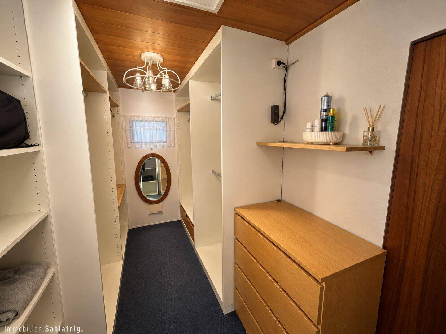 Begehbarer Kleiderschrank mit viel Stauraum, Holzdecke und einem ovalen Spiegel.