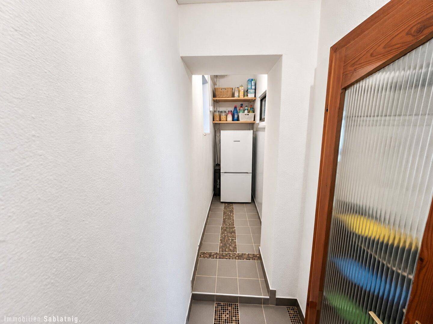 Langer Abstellraum mit Kühlschrank und Regalen, ideal für zusätzliche Lagerung.