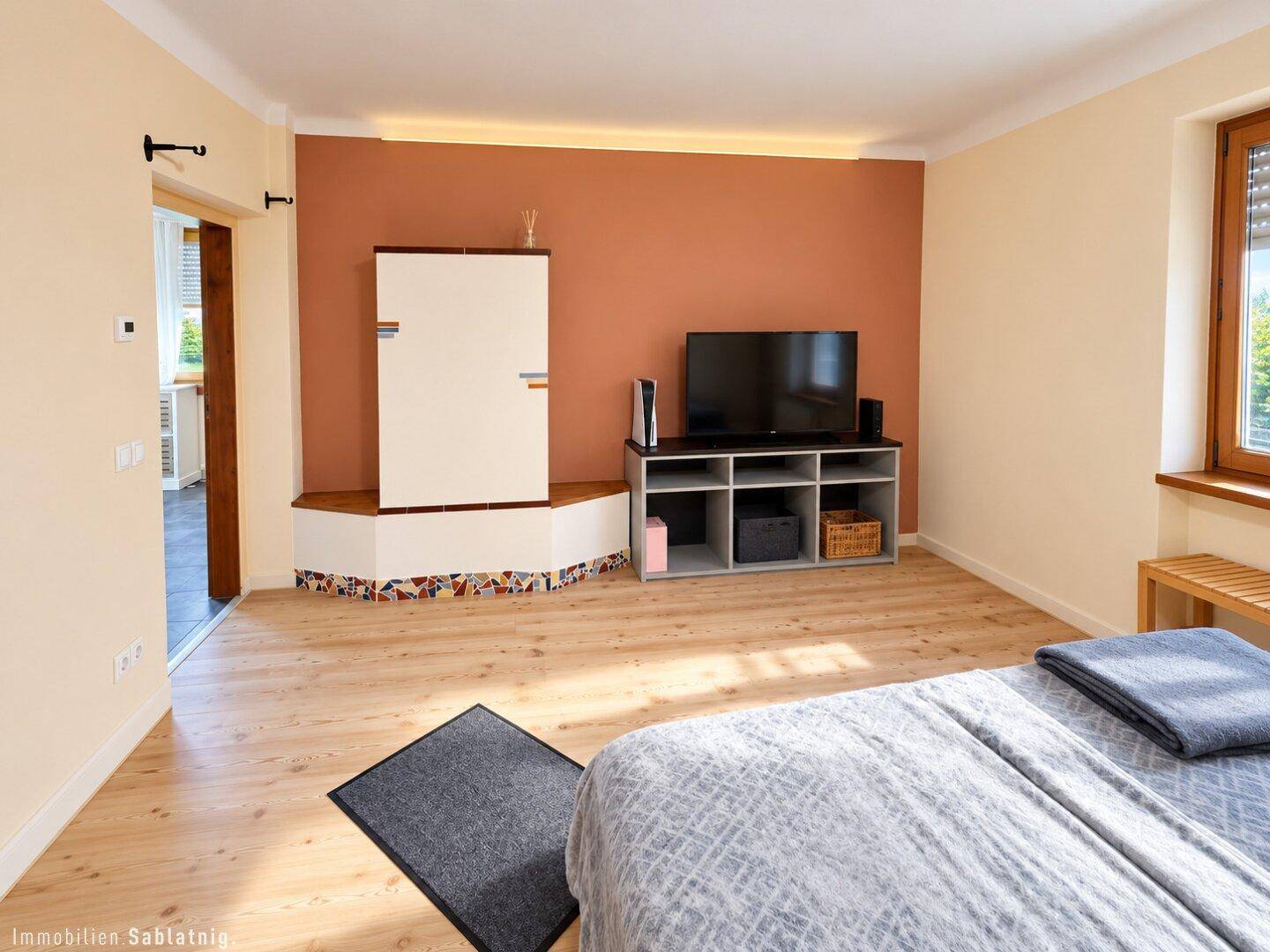 Gemütliches Schlafzimmer mit Holzboden, Kachelofen und farbiger Akzentwand.