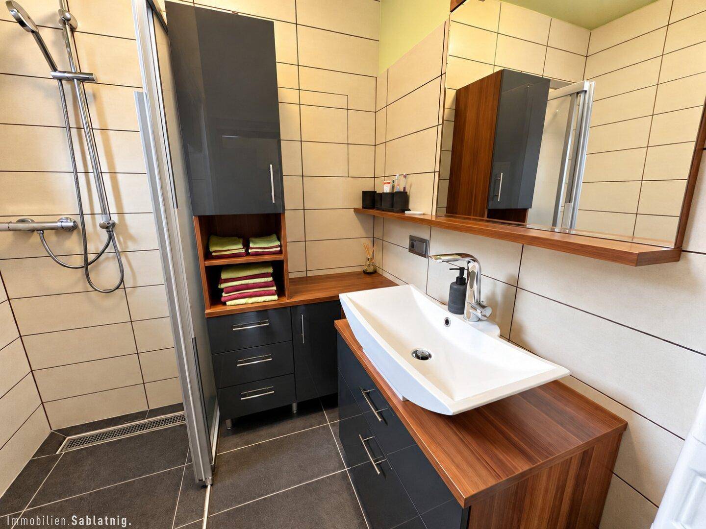 Modernes Badezimmer mit begehbarer Dusche, Waschtisch und dunklen Schränken.