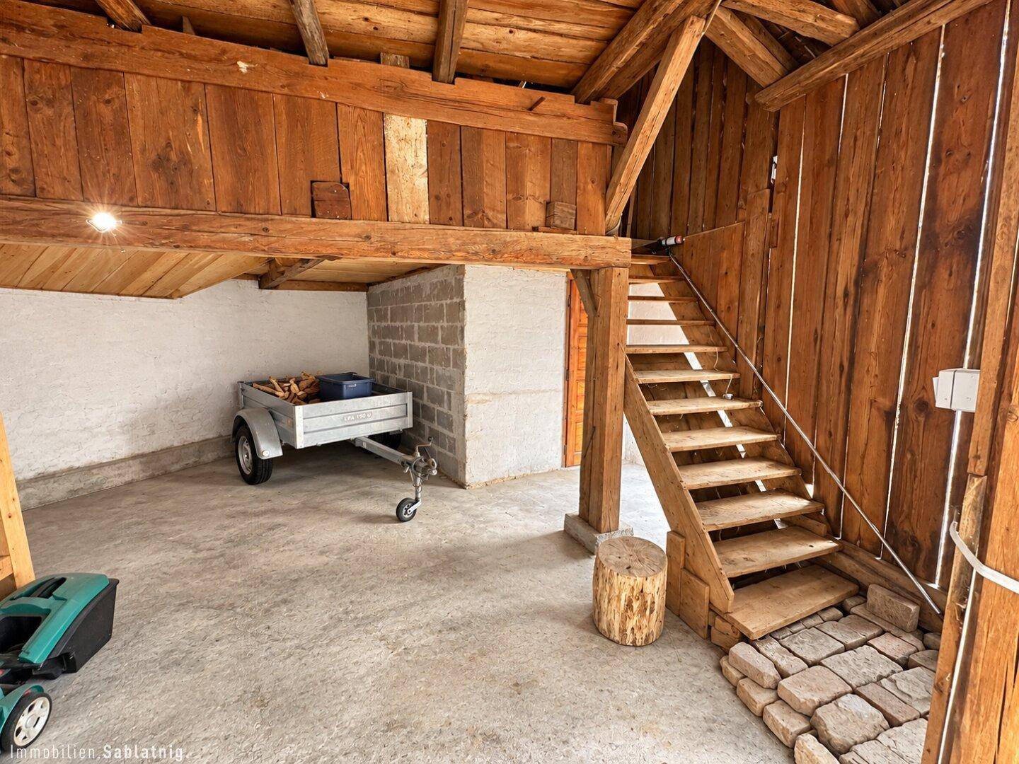 Rustikaler Scheunenbereich mit Holzbalken, Betonboden und Holztreppe.