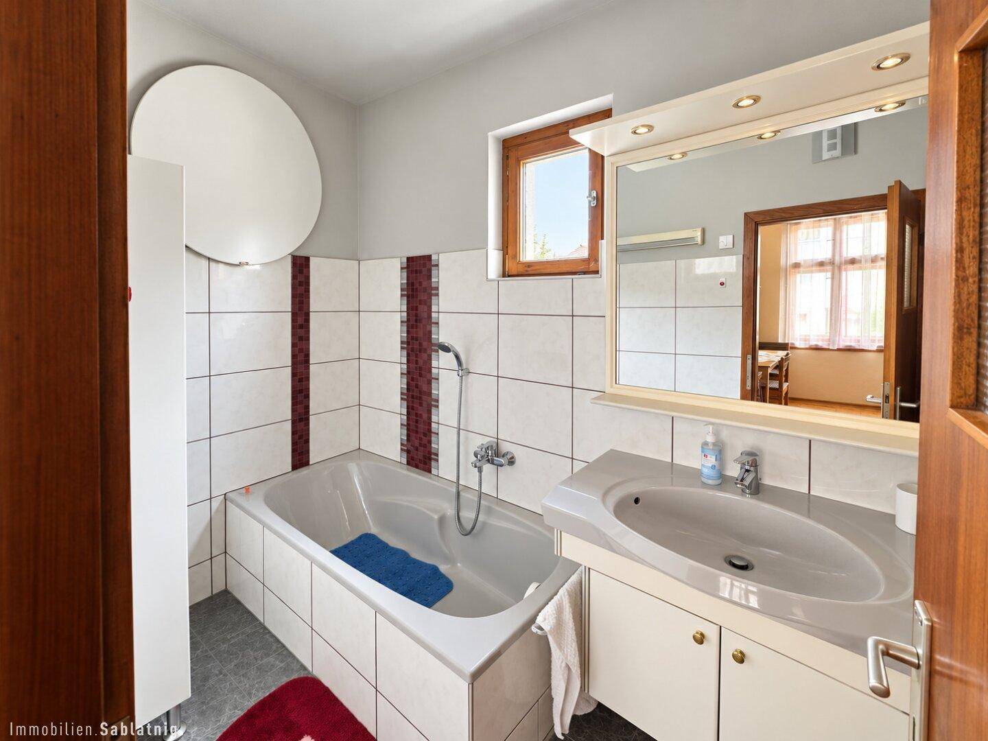 Badezimmer mit Badewanne, Waschtisch und weißen Fliesen mit roten Akzenten.