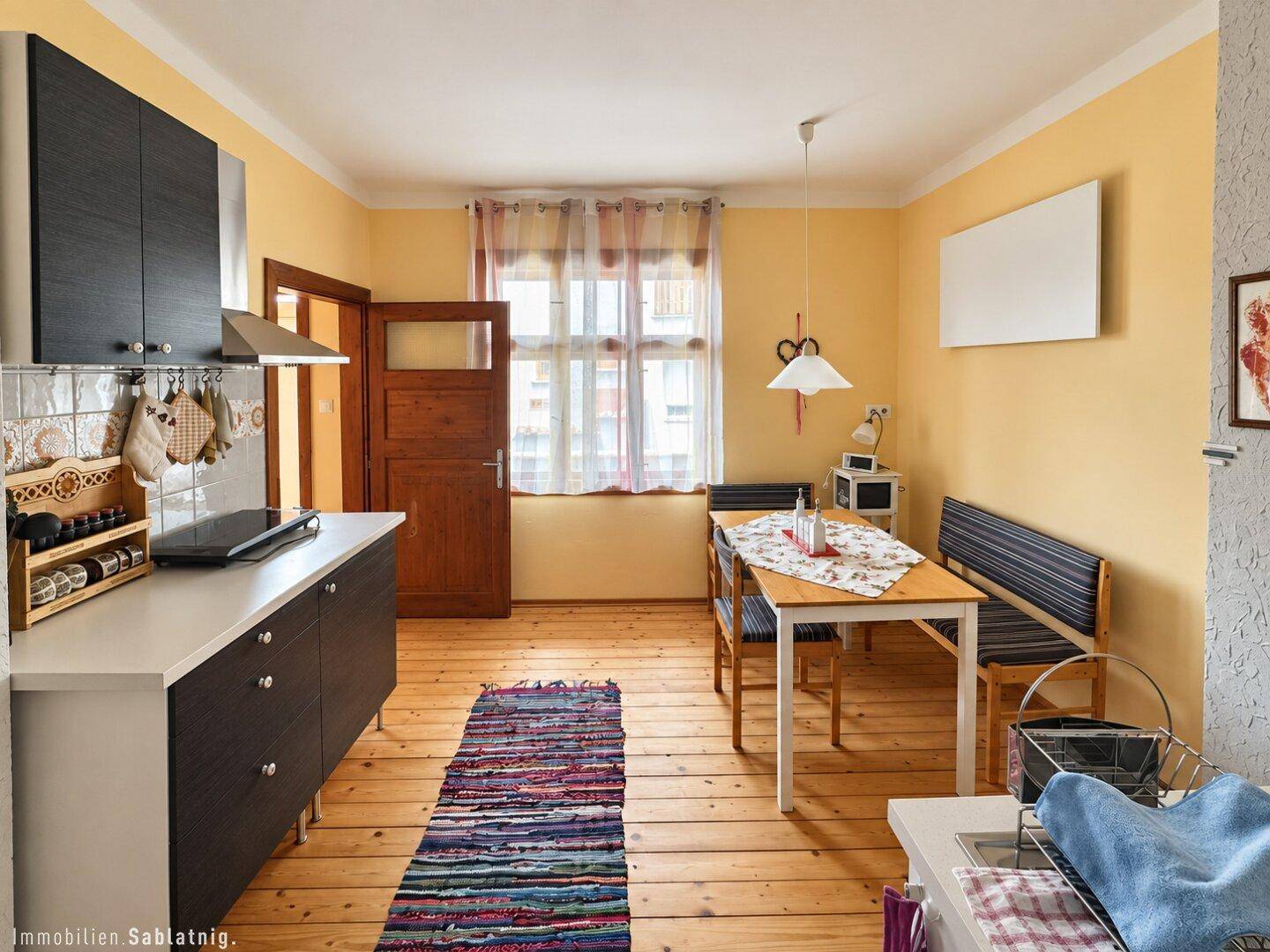 Helle Wohnküche mit Holzdielenboden, Esstisch und modernen Küchenschränken.