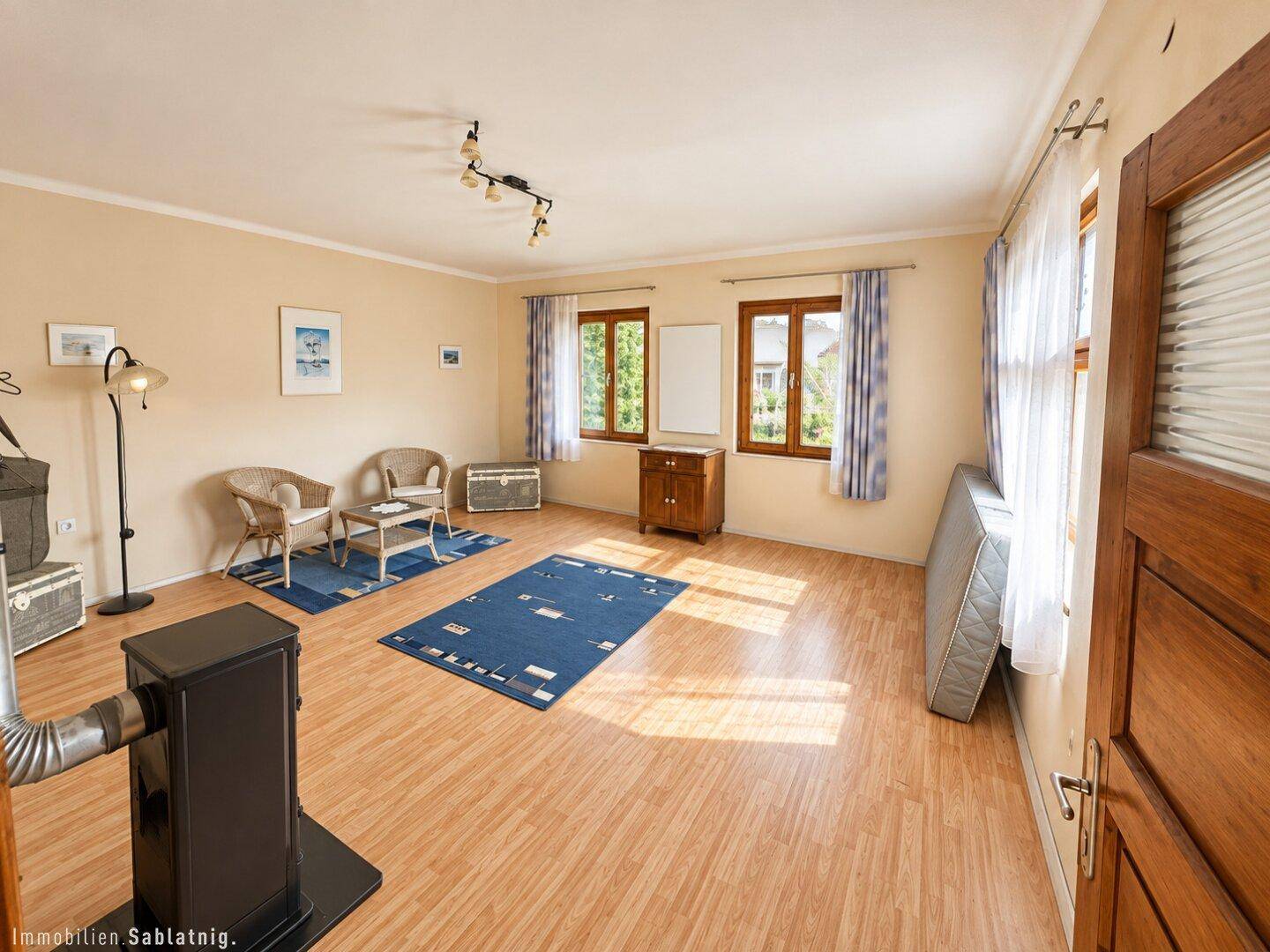 Geräumiges Wohnzimmer mit Laminatboden, Holzofen und Blick ins Grüne.