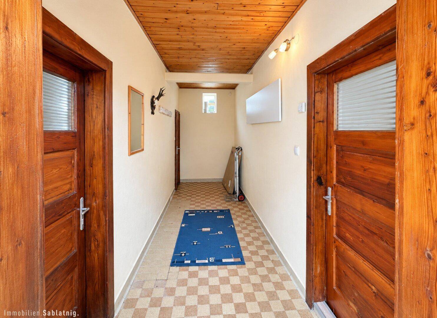 Langer Flur mit Holzdecke, kariertem Fliesenboden und rustikalen Holztüren.
