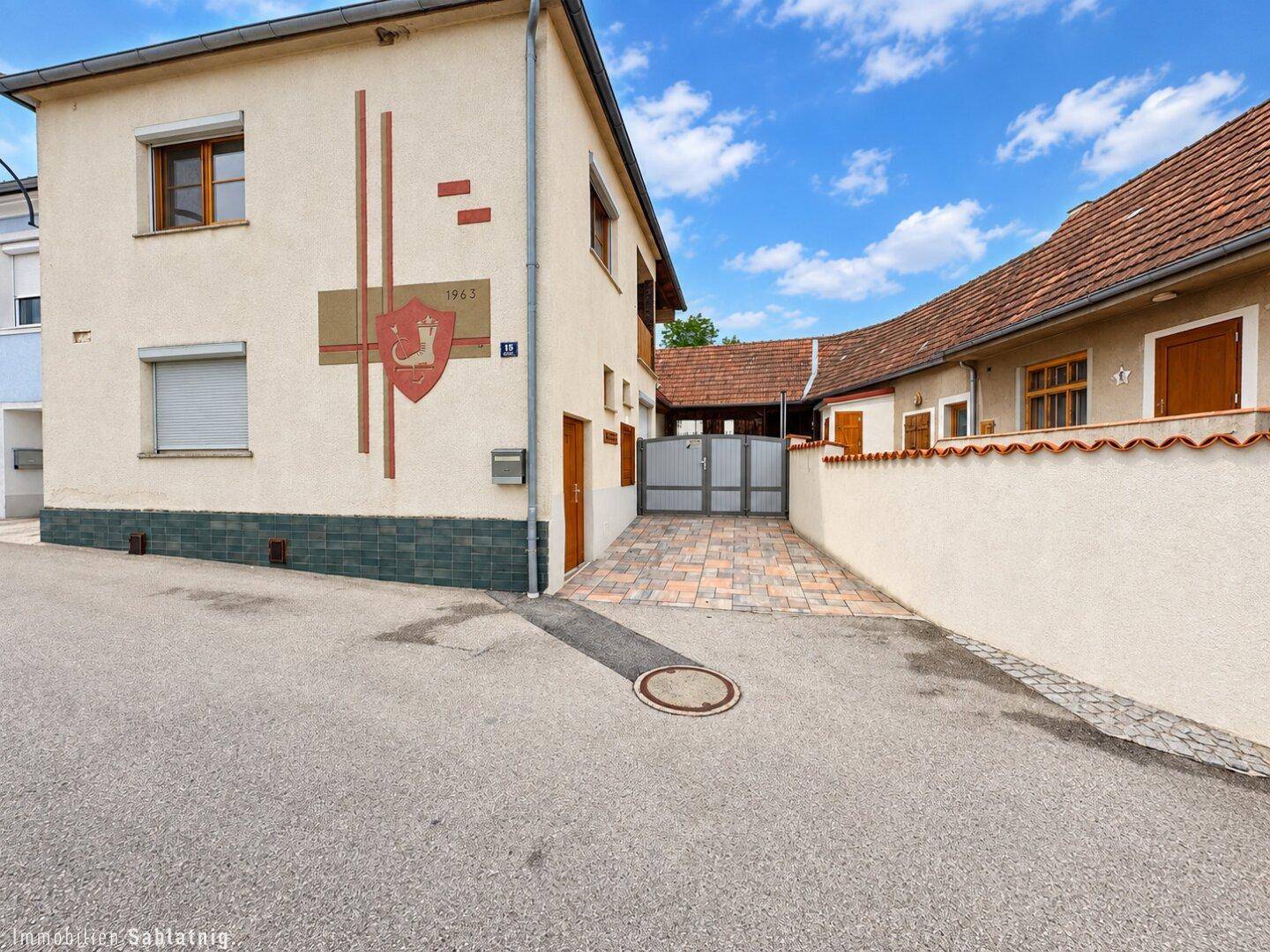 Ansicht des Hauses von der Straße mit gepflasterter Einfahrt und dekorativem Wappen.
