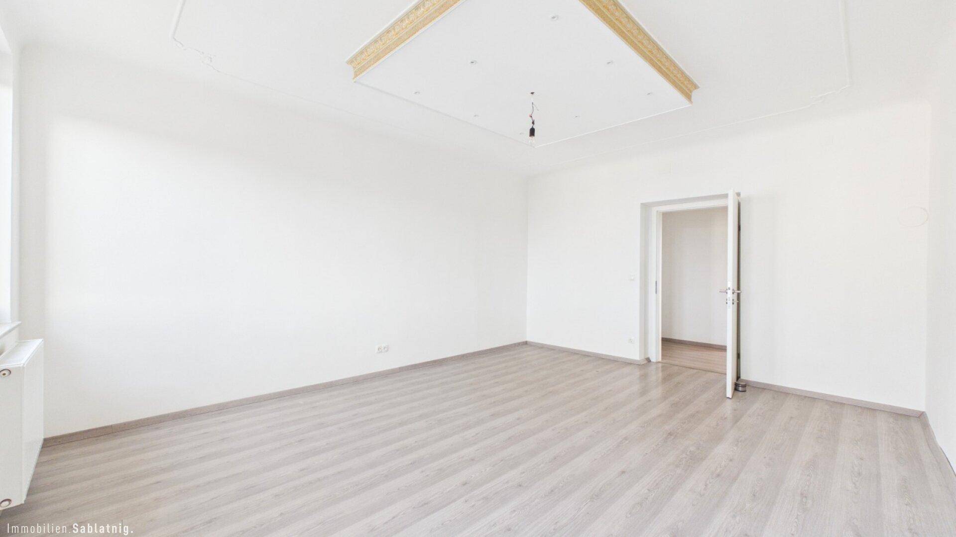 Helles, unmöbliertes Zimmer mit Laminatboden und einem Fenster, das viel Licht spendet.