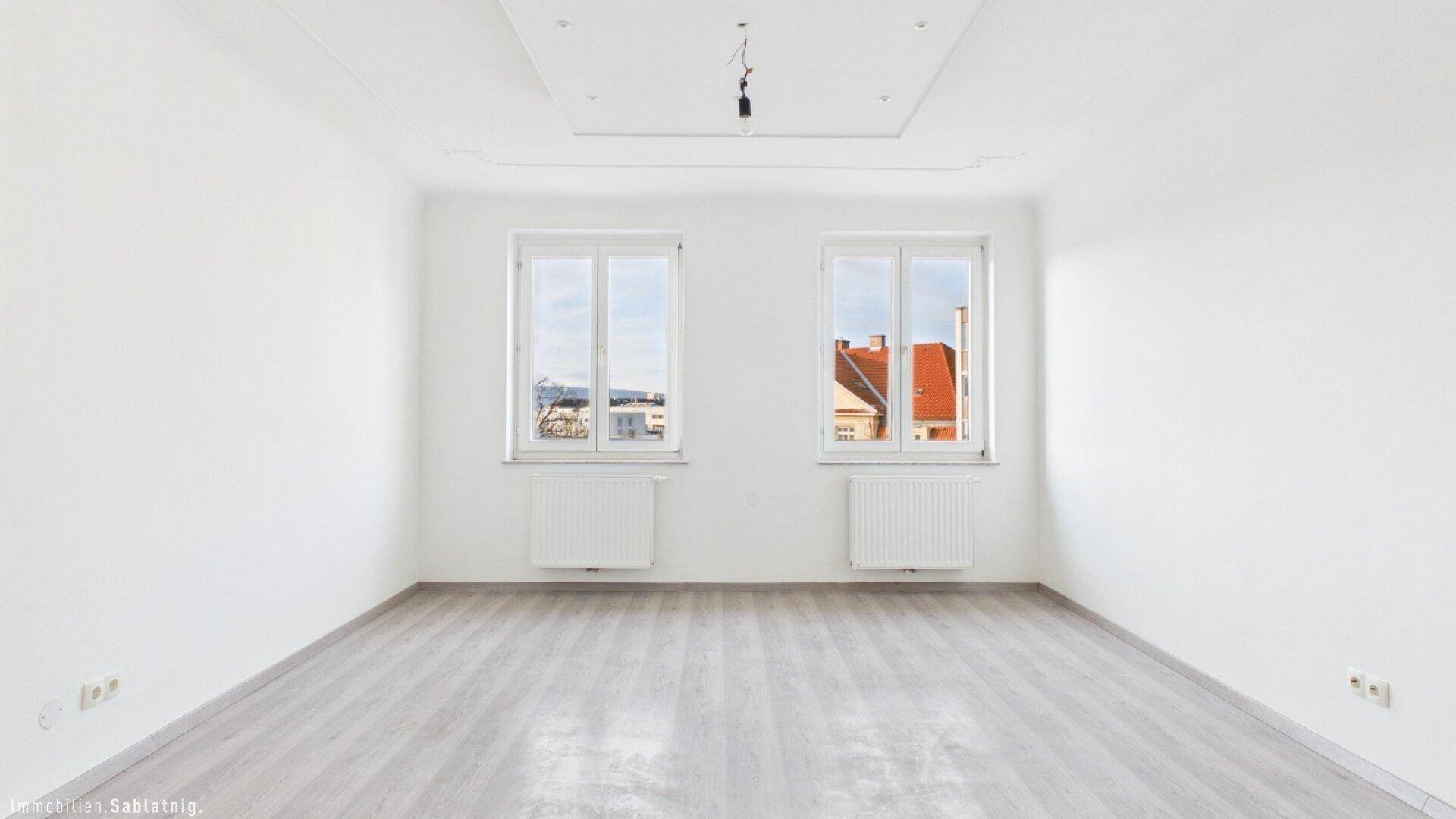 Lichtdurchflutetes Zimmer mit hellem Laminatboden und Blick nach draußen, unmöbliert.