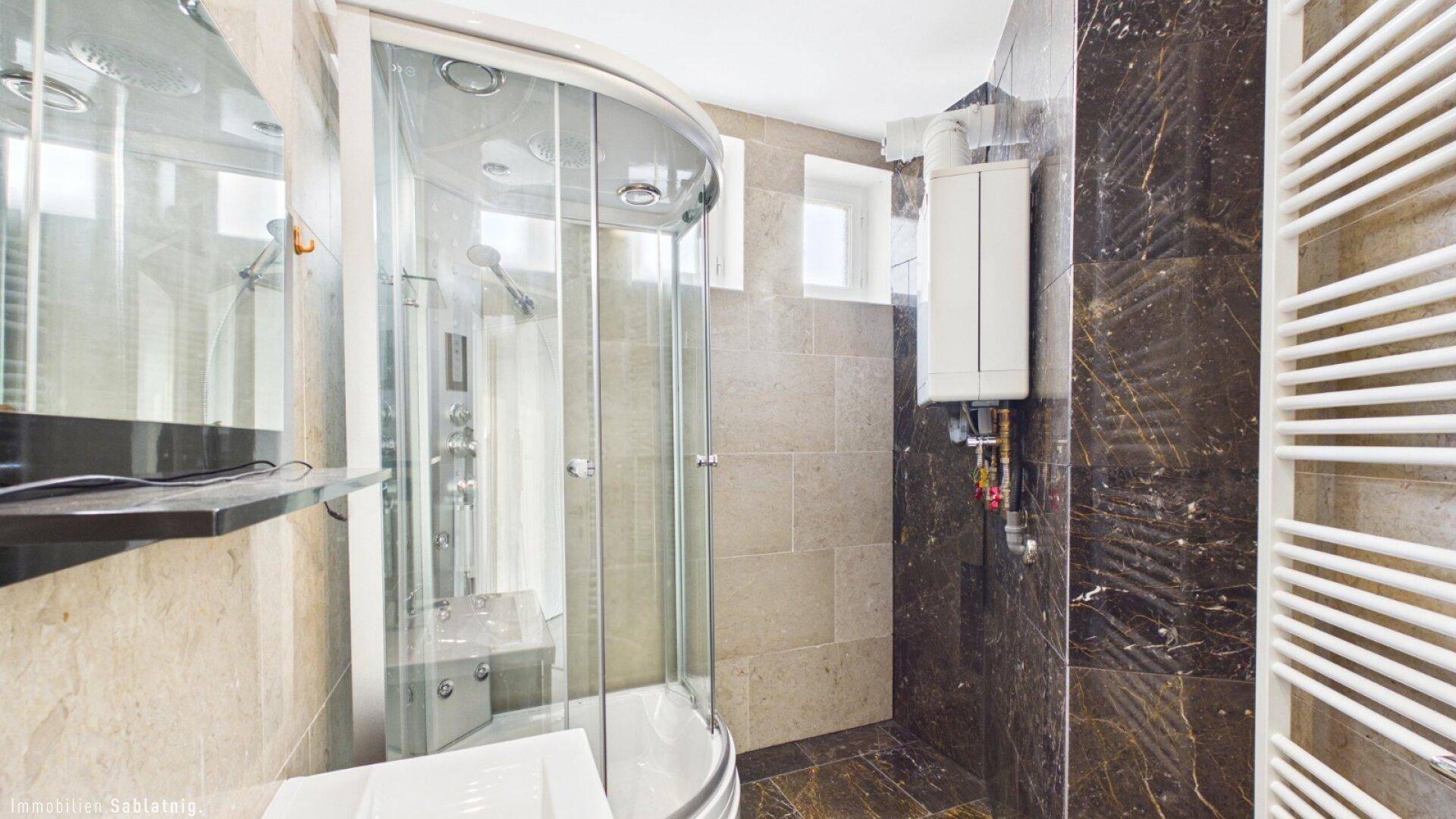 Elegantes Badezimmer mit runder Duschkabine, dunklen Fliesen und beheiztem Handtuchhalter.