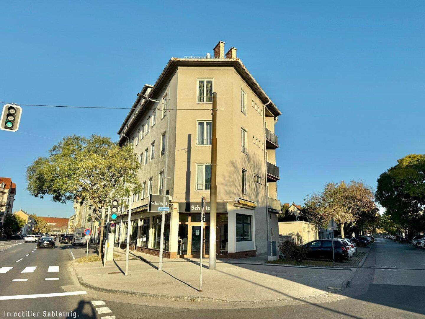 Eckgebäude mit Geschäften im Erdgeschoss und Wohnungen darüber, an einer belebten Straße.