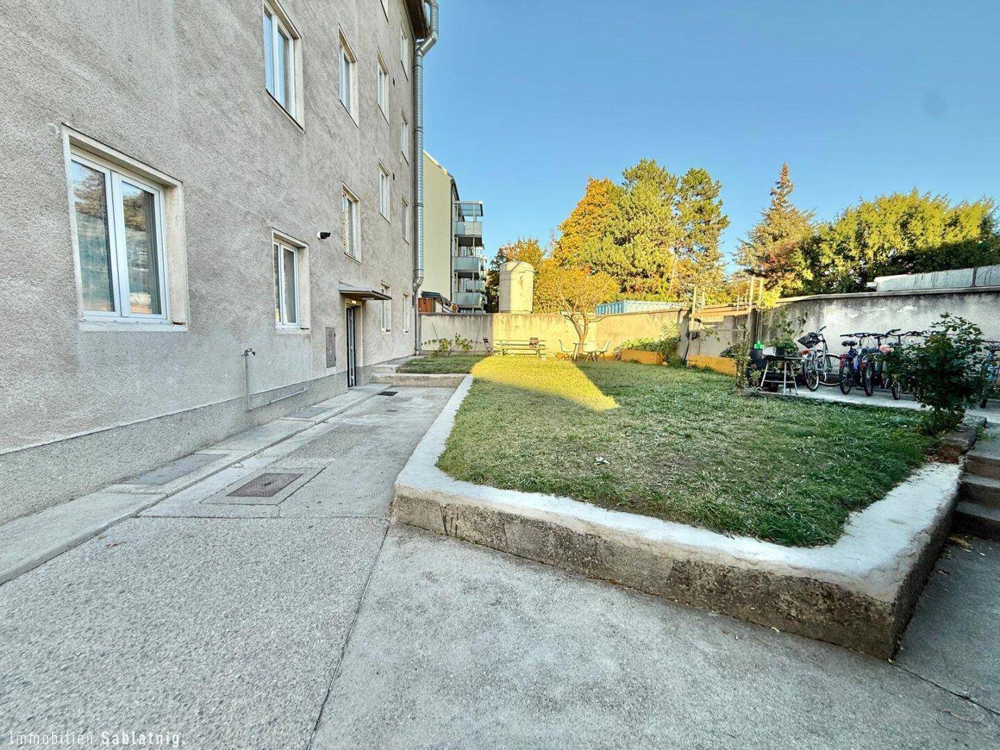 Gemeinschaftsgarten mit Rasenfläche und Fahrradabstellplätzen hinter dem Gebäude.