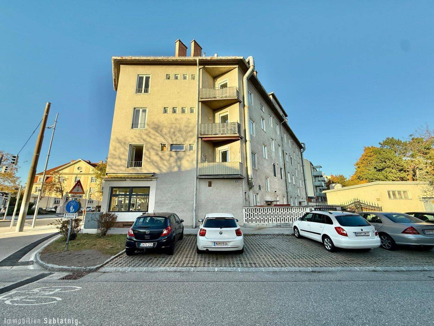 Mehrstöckiges Wohngebäude mit Balkonen und Parkplätzen an der Straße.