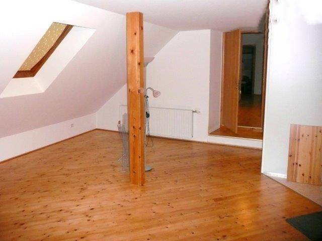 Heller Dachraum mit Holzboden, schrägen Wänden, sichtbarem Holzbalken und Zugang zu weiteren Räumen.