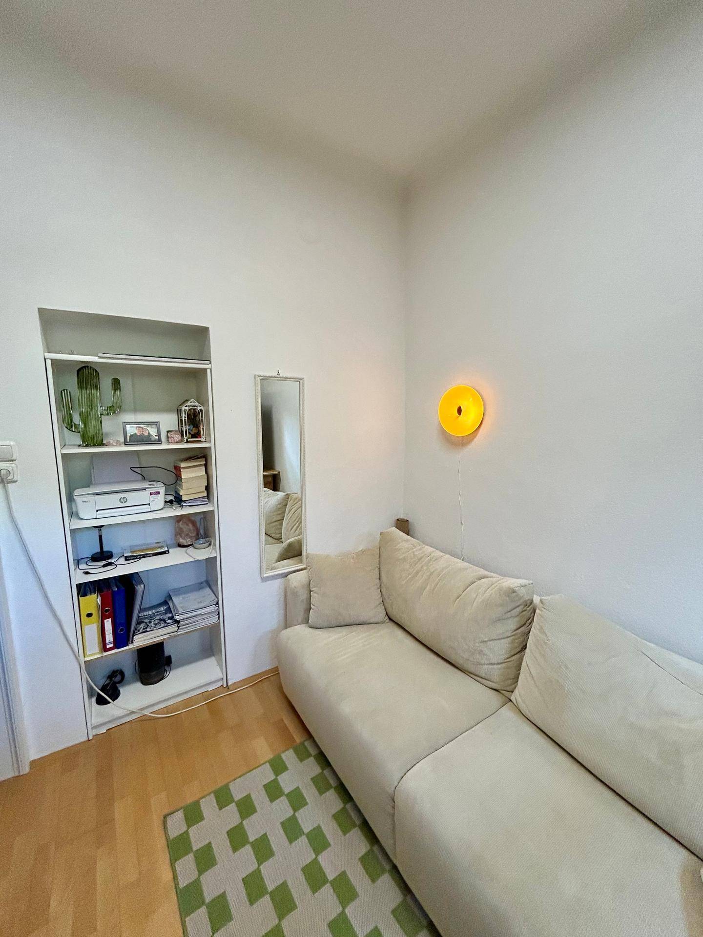 Heller Raum mit bequemem Sofa, integriertem Regal und einem kleinen Fenster.