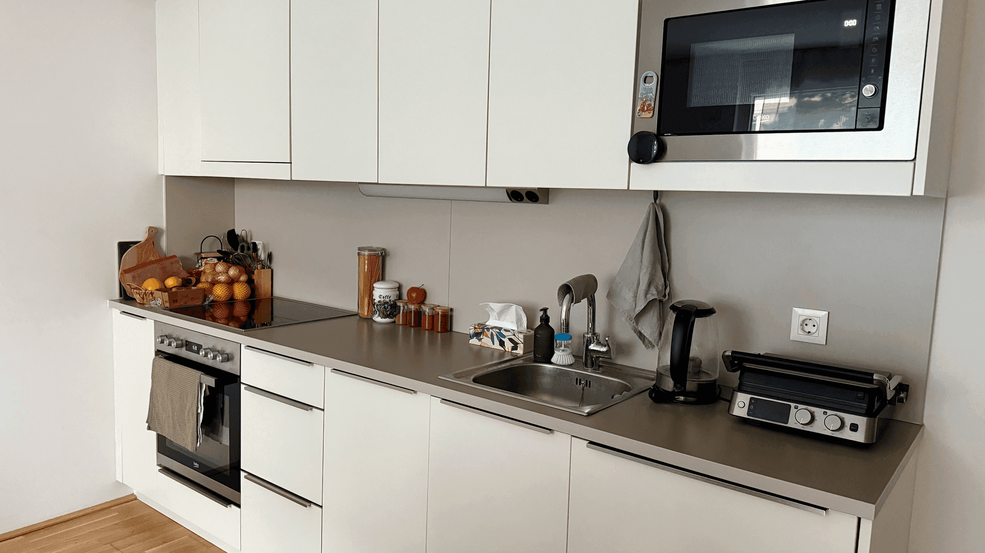Moderne Einbauküche mit weißen Schränken, grauer Arbeitsplatte und integrierten Geräten.