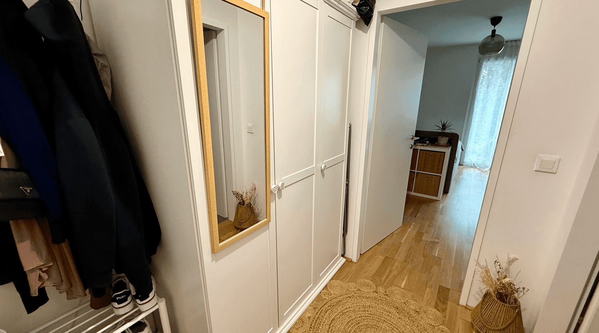 Eingangsbereich mit weißem Kleiderschrank, Spiegel und Blick in den angrenzenden Wohnbereich.