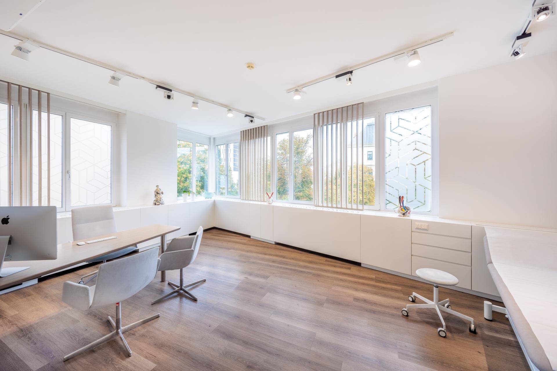Helles Büro oder Behandlungszimmer mit zwei Schreibtischen, Bürostühlen und großen Fenstern mit Jalousien.