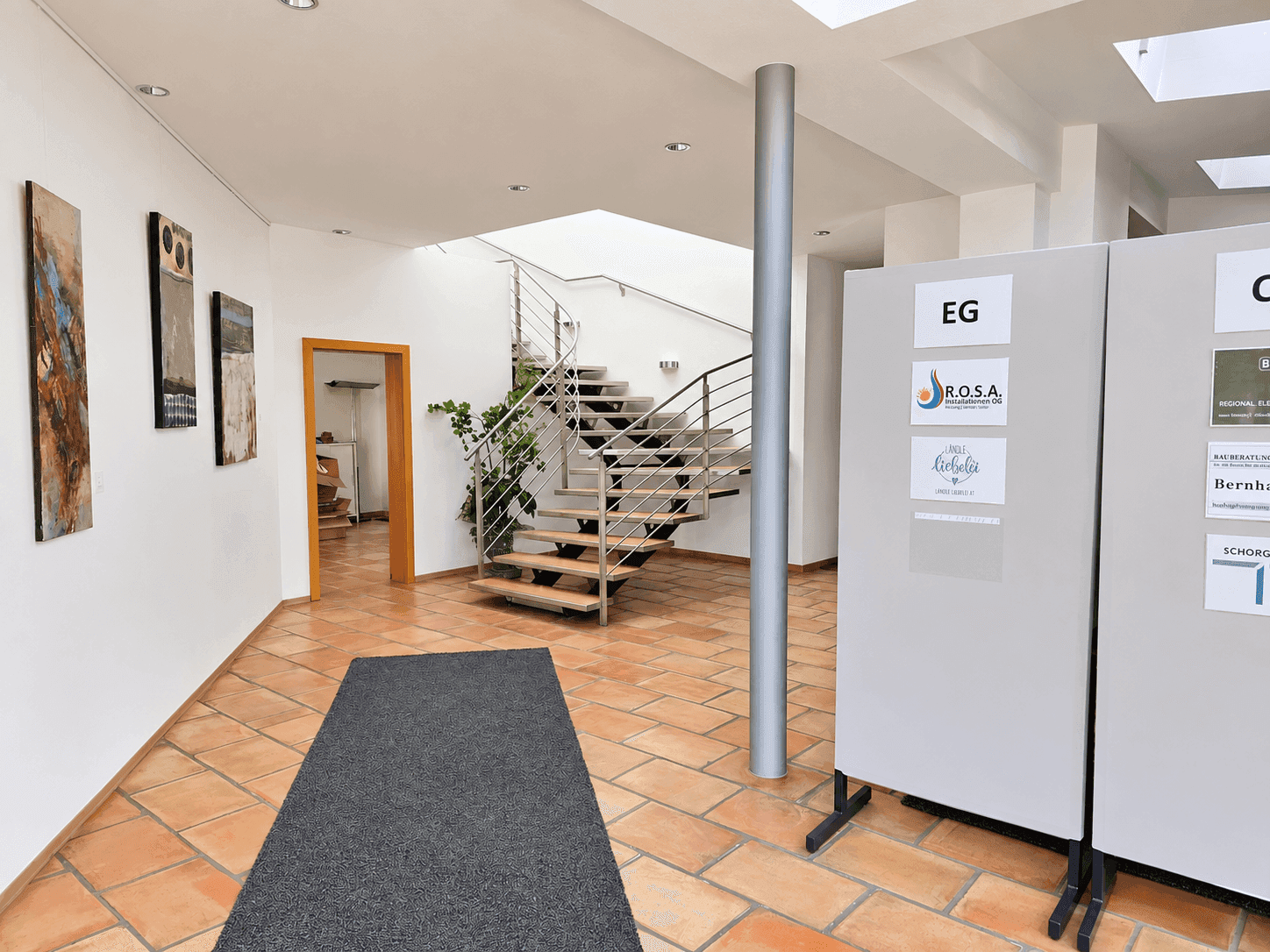 Geräumiger Flur mit moderner Holztreppe, Metallgeländer und Kunstwerken an den weißen Wänden.