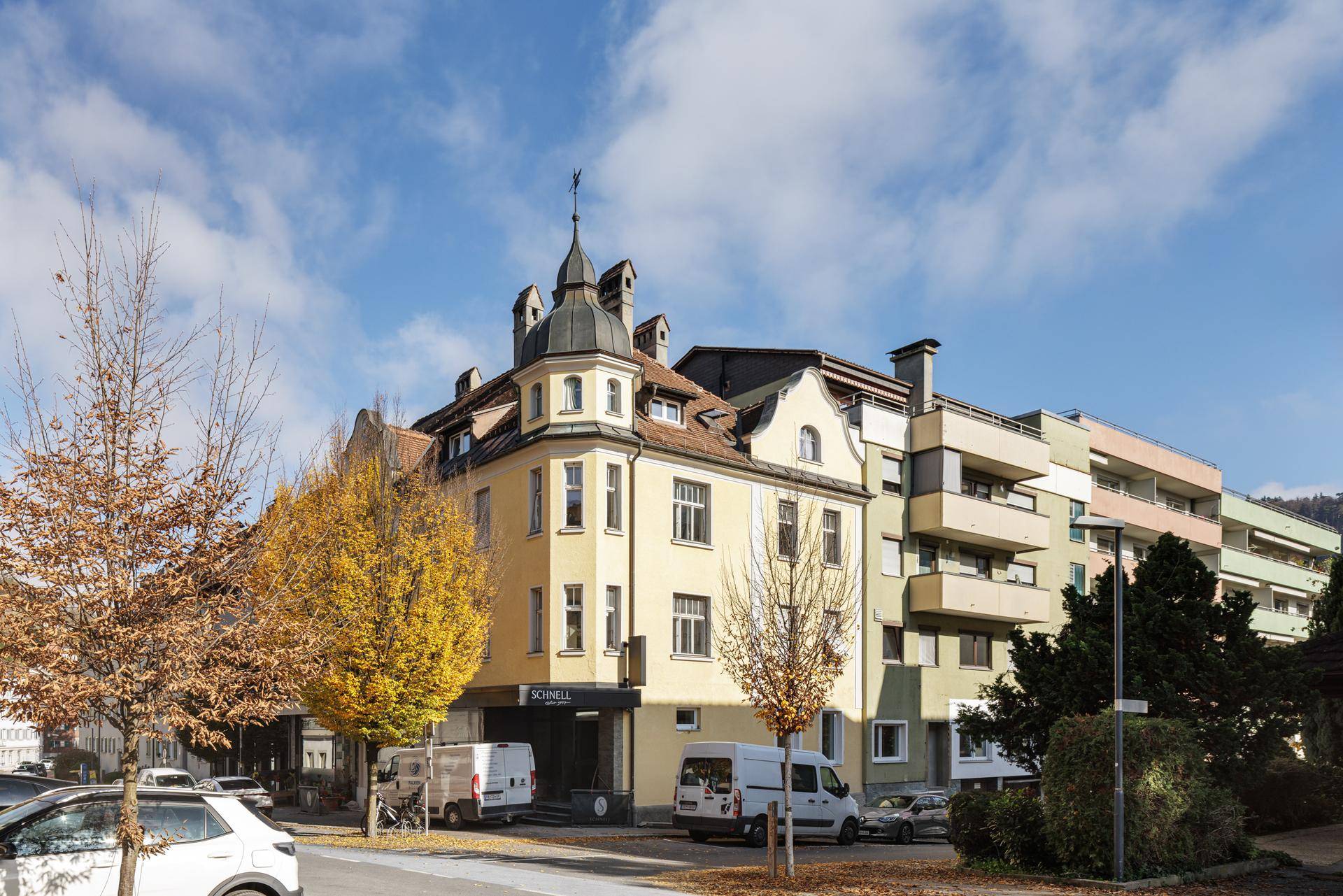 Historisches Gebäude mit markantem Turm und modernen Anbauten in städtischer Umgebung.