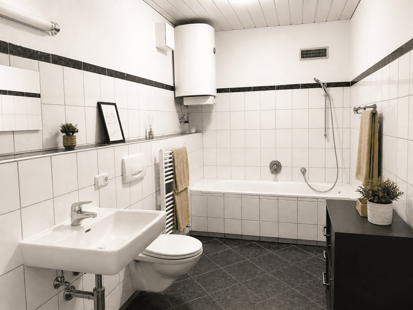 Gefliestes Badezimmer mit Badewanne, WC, Waschbecken und beheiztem Handtuchhalter.