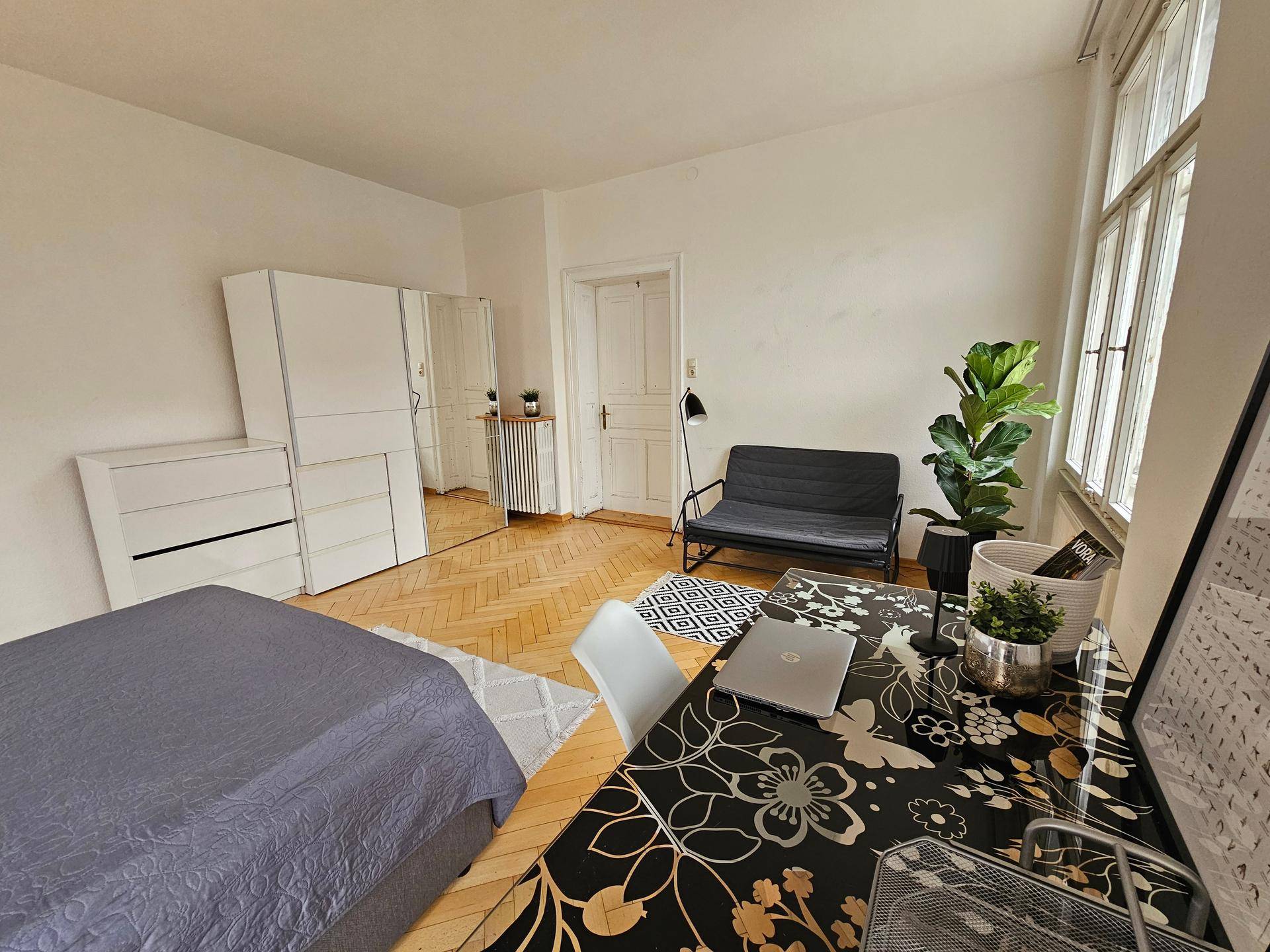 Helles Schlafzimmer mit Fischgrätparkett, weißem Kleiderschrank und modernem Schreibtisch.