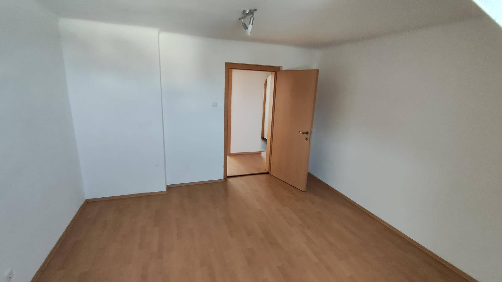 Leeres Schlafzimmer mit Laminatboden, weißen Wänden und Holztür.