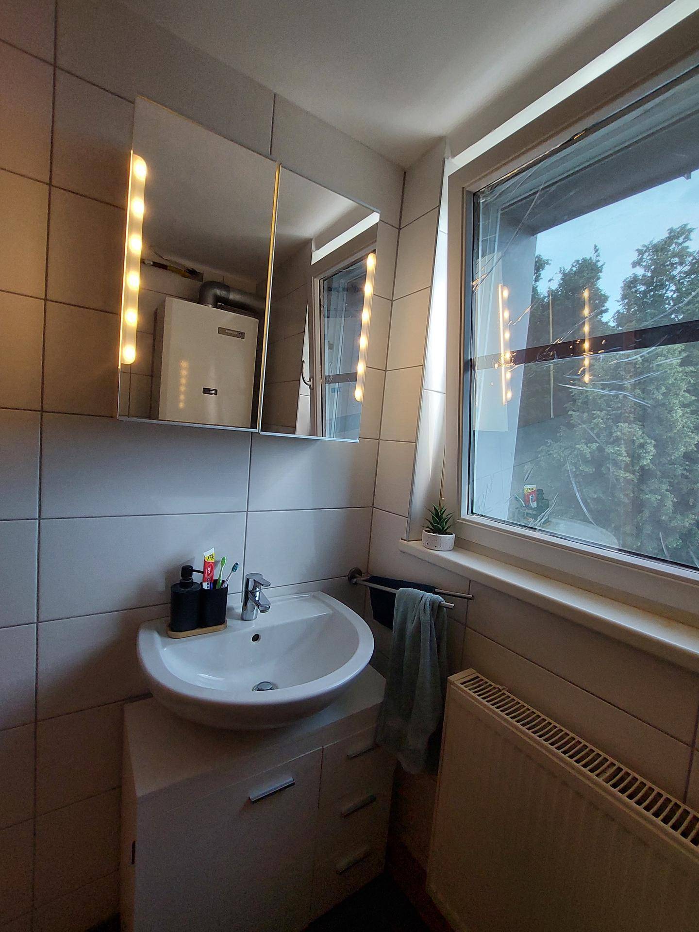 Badezimmer mit Waschbecken, Spiegelschrank und Fenster, das Tageslicht hereinlässt.