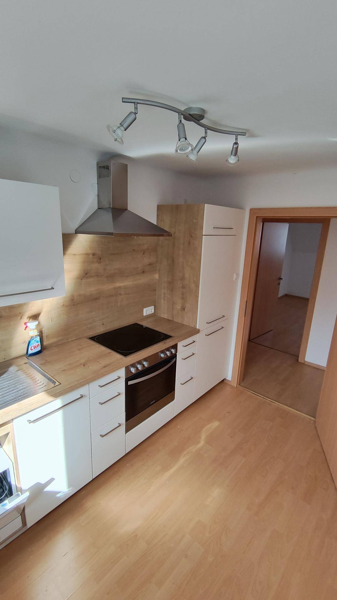 Helle Küche mit Holzoptik-Arbeitsplatte, Einbaugeräten und Zugang zu weiteren Räumen.