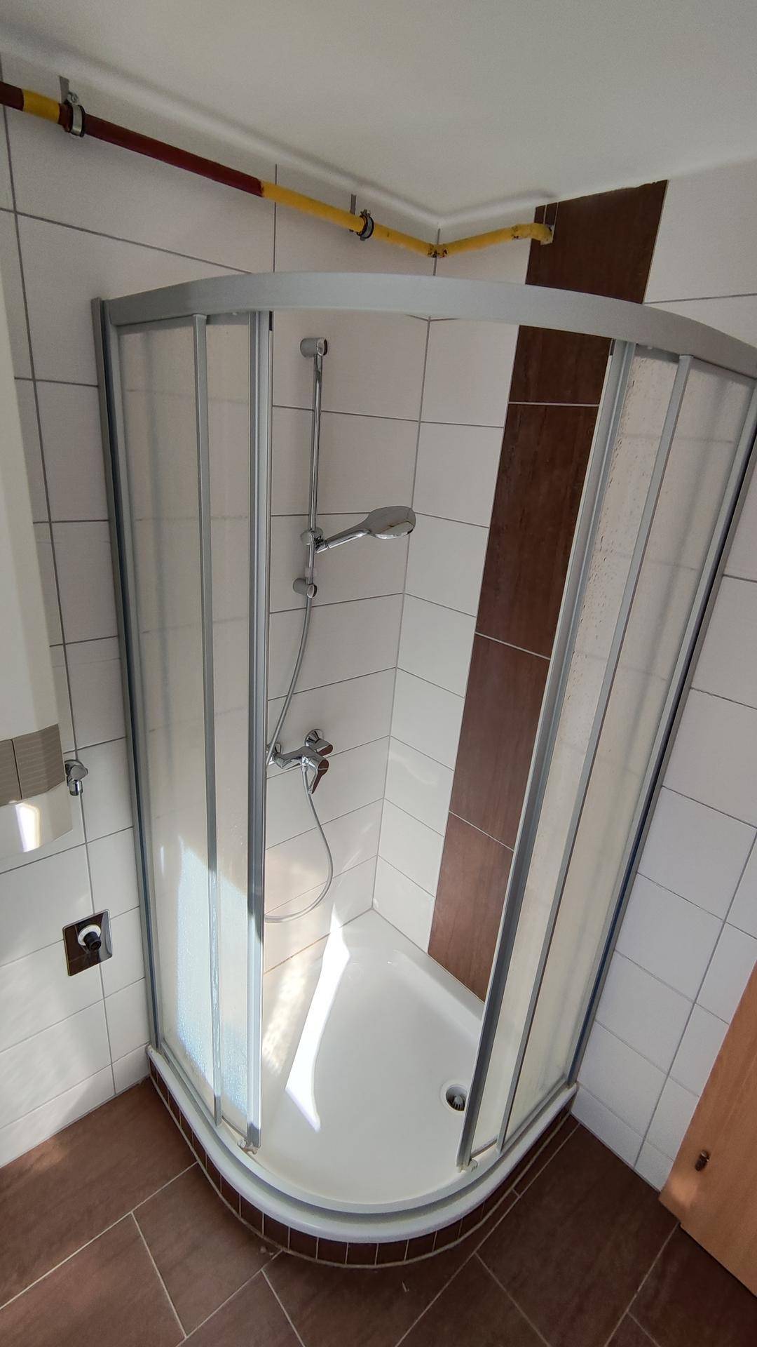 Badezimmer mit Eckdusche, weißen Fliesen und braunen Akzentstreifen.