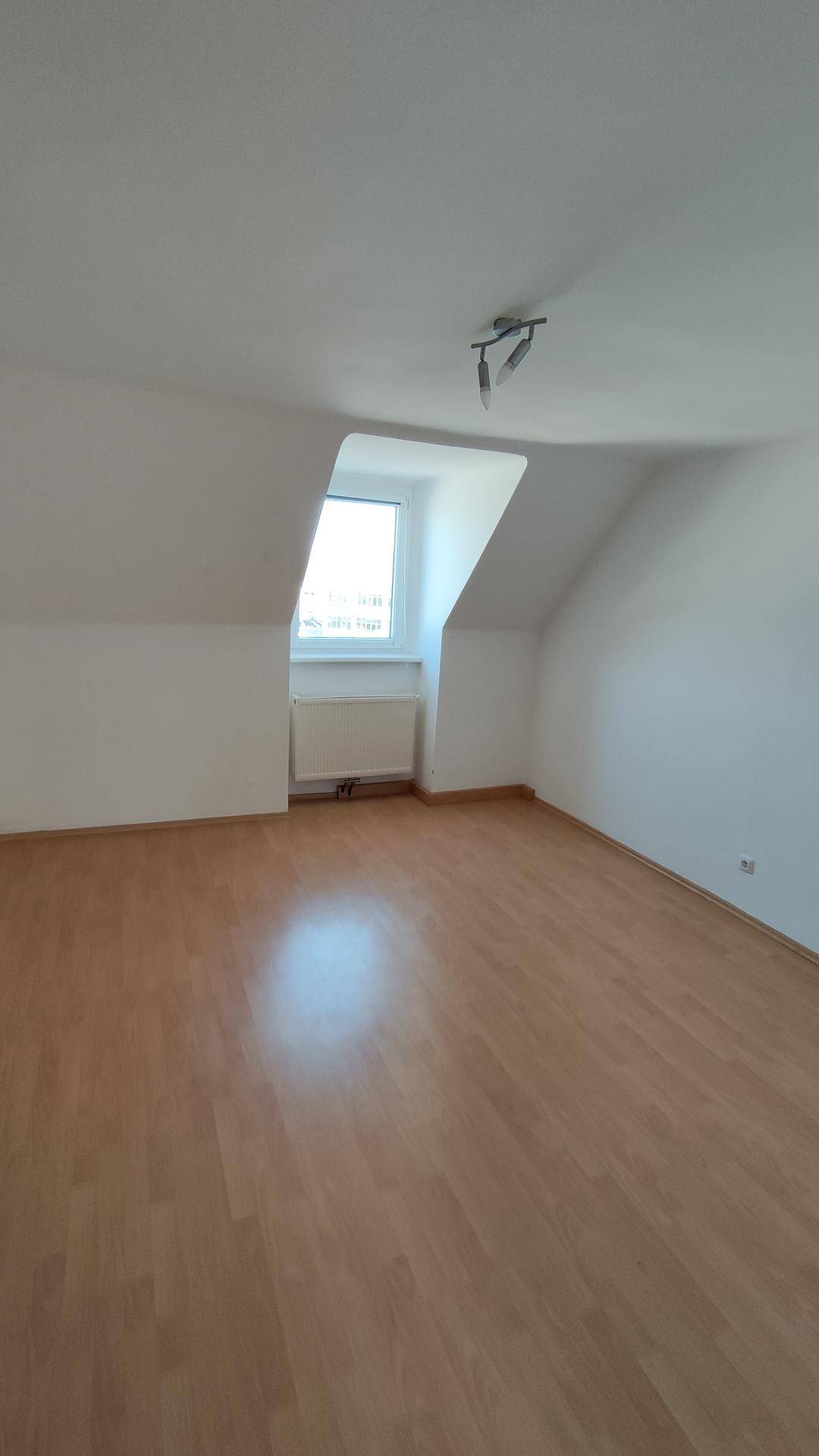 Dachgeschosszimmer mit Laminatboden, schräger Wand und einem Fenster.