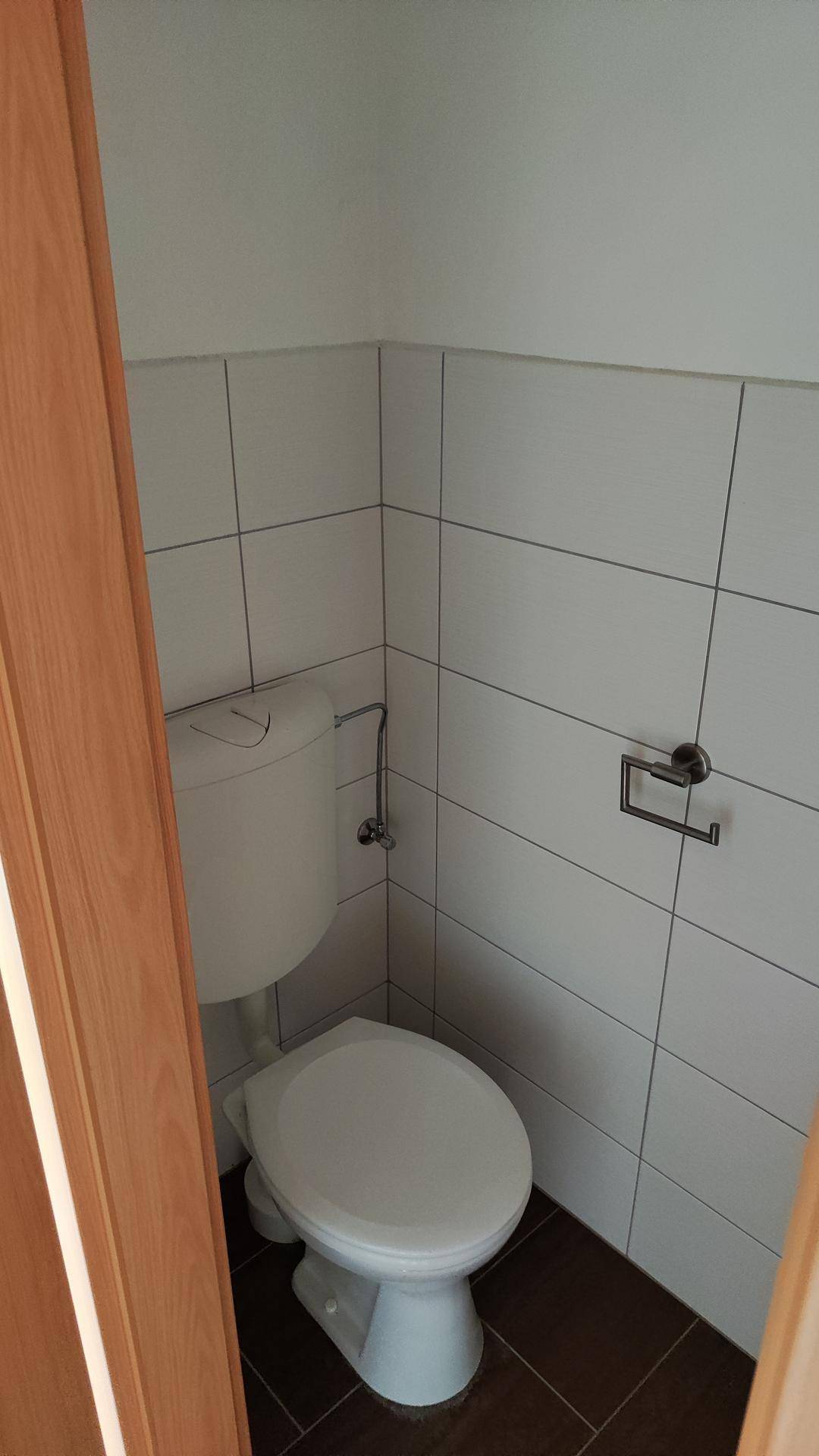 Separate Toilette mit weißen Fliesen, WC und dunklem Fliesenboden.