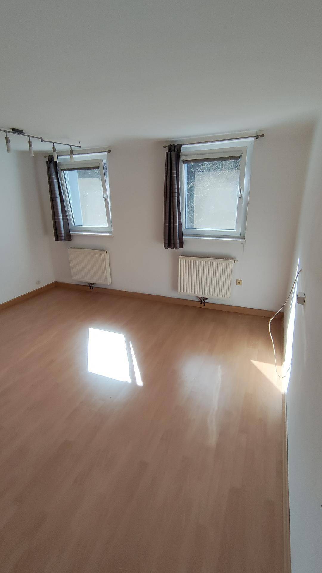 Heller Raum mit Laminatboden, zwei Fenstern und viel natürlichem Lichteinfall.