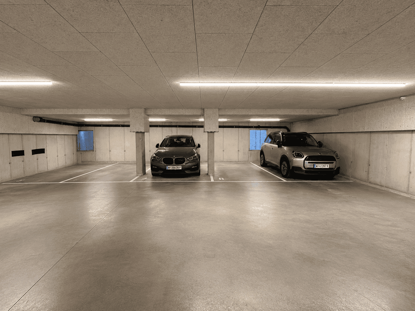 Tiefgarage mit zwei geparkten Autos und moderner Beleuchtung.