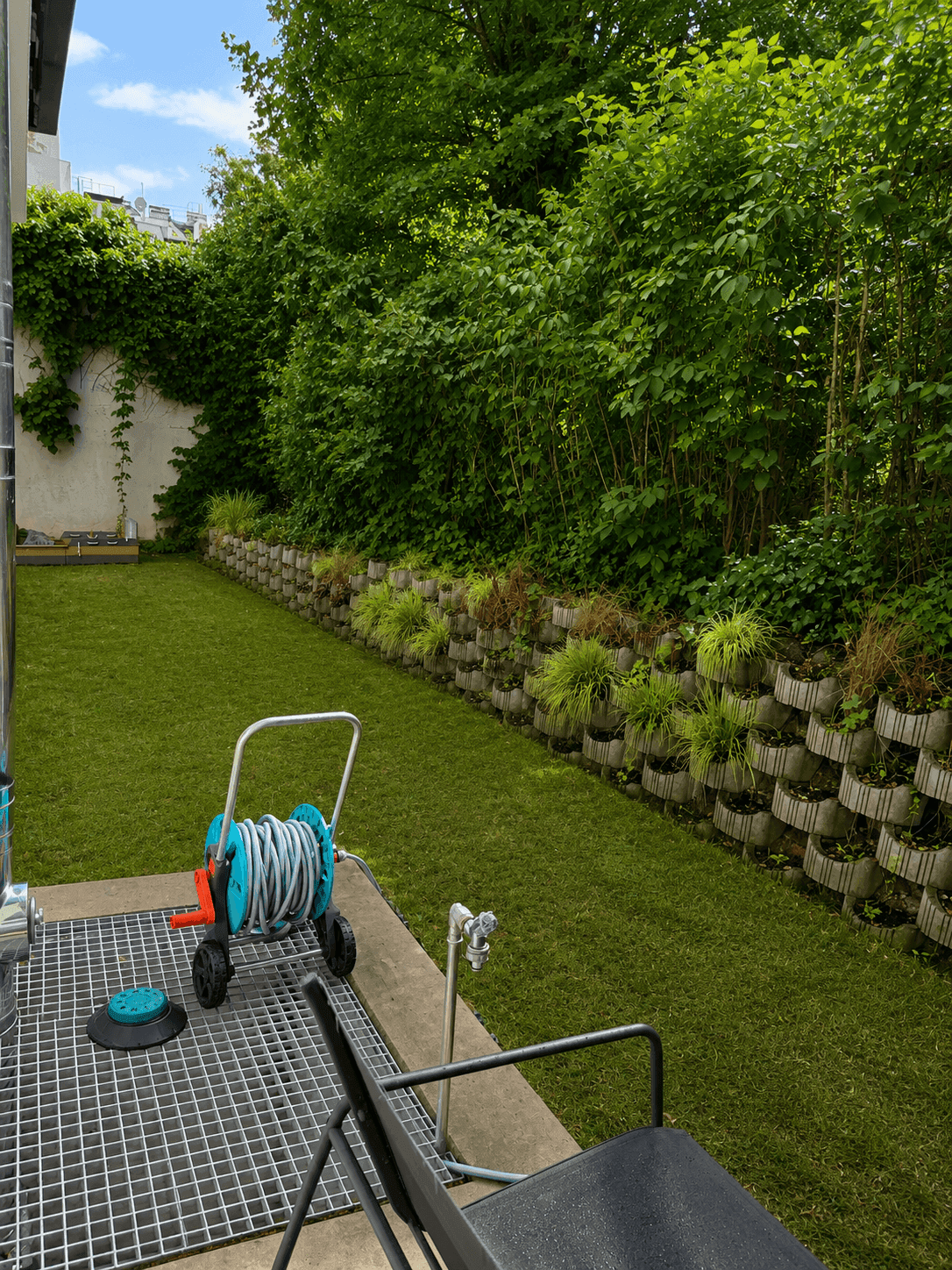Gartenbereich mit Kunstrasen, Gartenschlauch und Wasseranschluss.