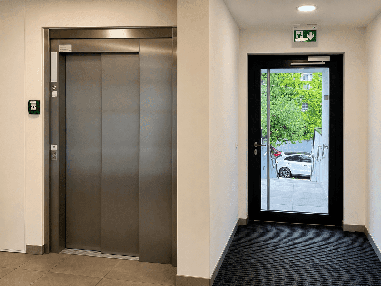 Heller Flur mit modernem Aufzug und Ausgangstür ins Freie.
