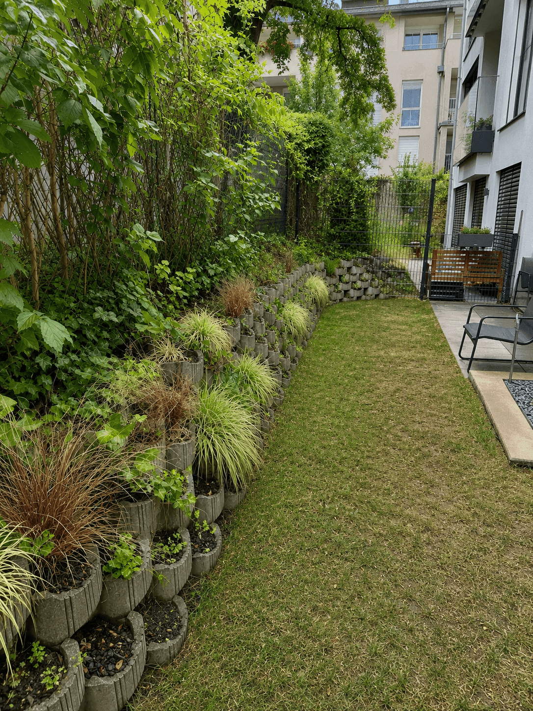 Gepflegter Gartenbereich mit Rasenfläche und bepflanzter Stützmauer.