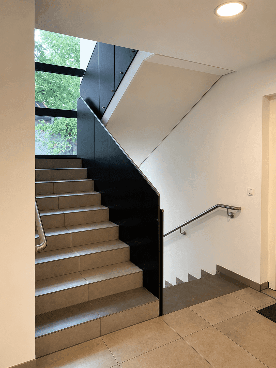 Modernes Treppenhaus mit großen Fenstern, die viel Tageslicht hereinlassen.