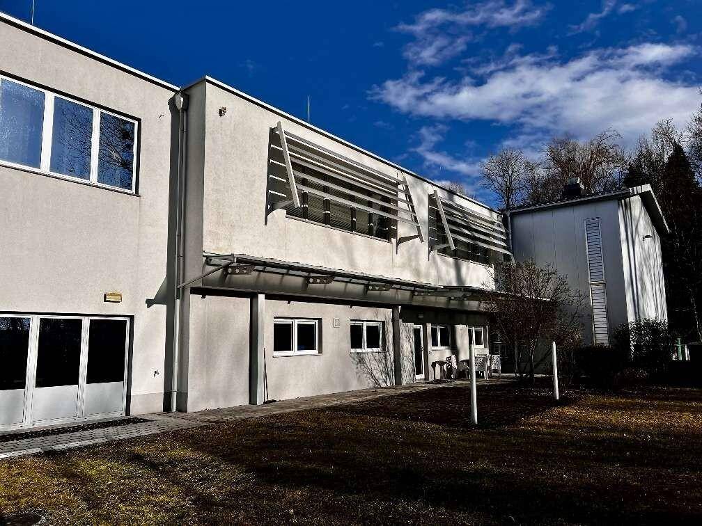 Außenansicht eines modernen Gebäudes mit großen Fenstern und Sonnenschutzlamellen unter blauem Himmel.