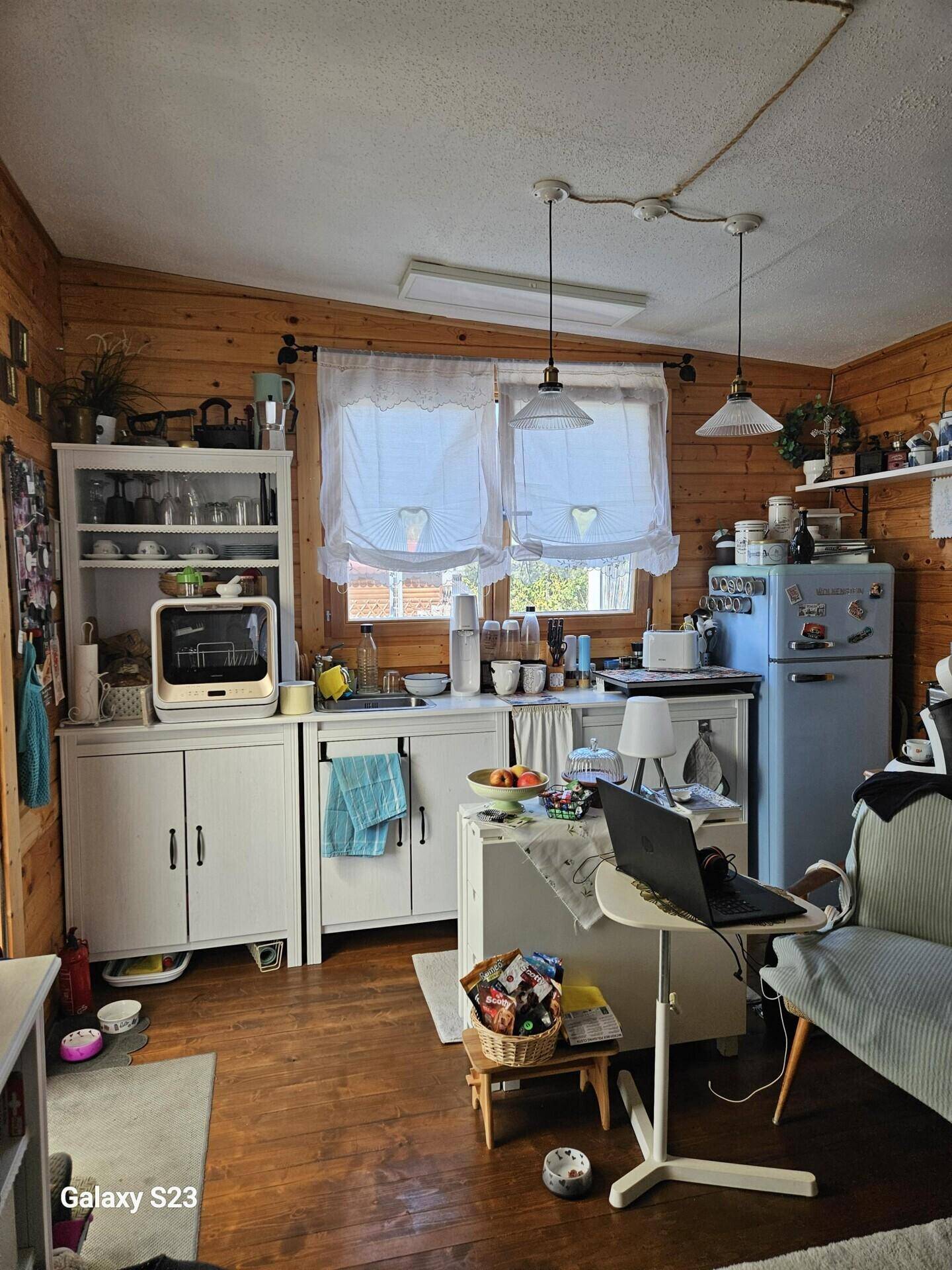 Gemütliche Holzküche mit weißen Schränken, kleinem Kühlschrank und Blick nach draußen.