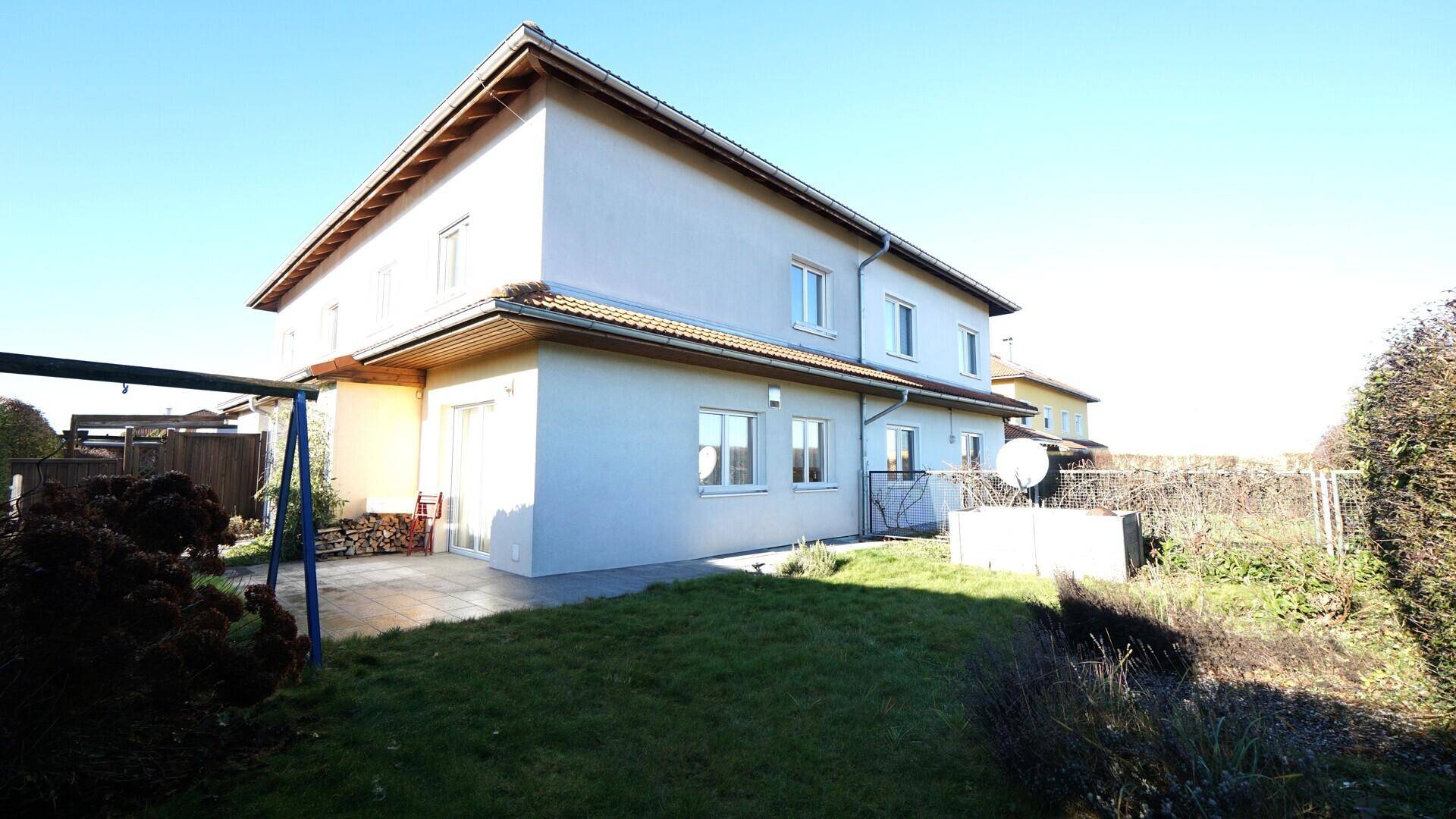 Hinterhof mit Rasenfläche, Schaukel und Terrasse am Haus, umgeben von Hecken.