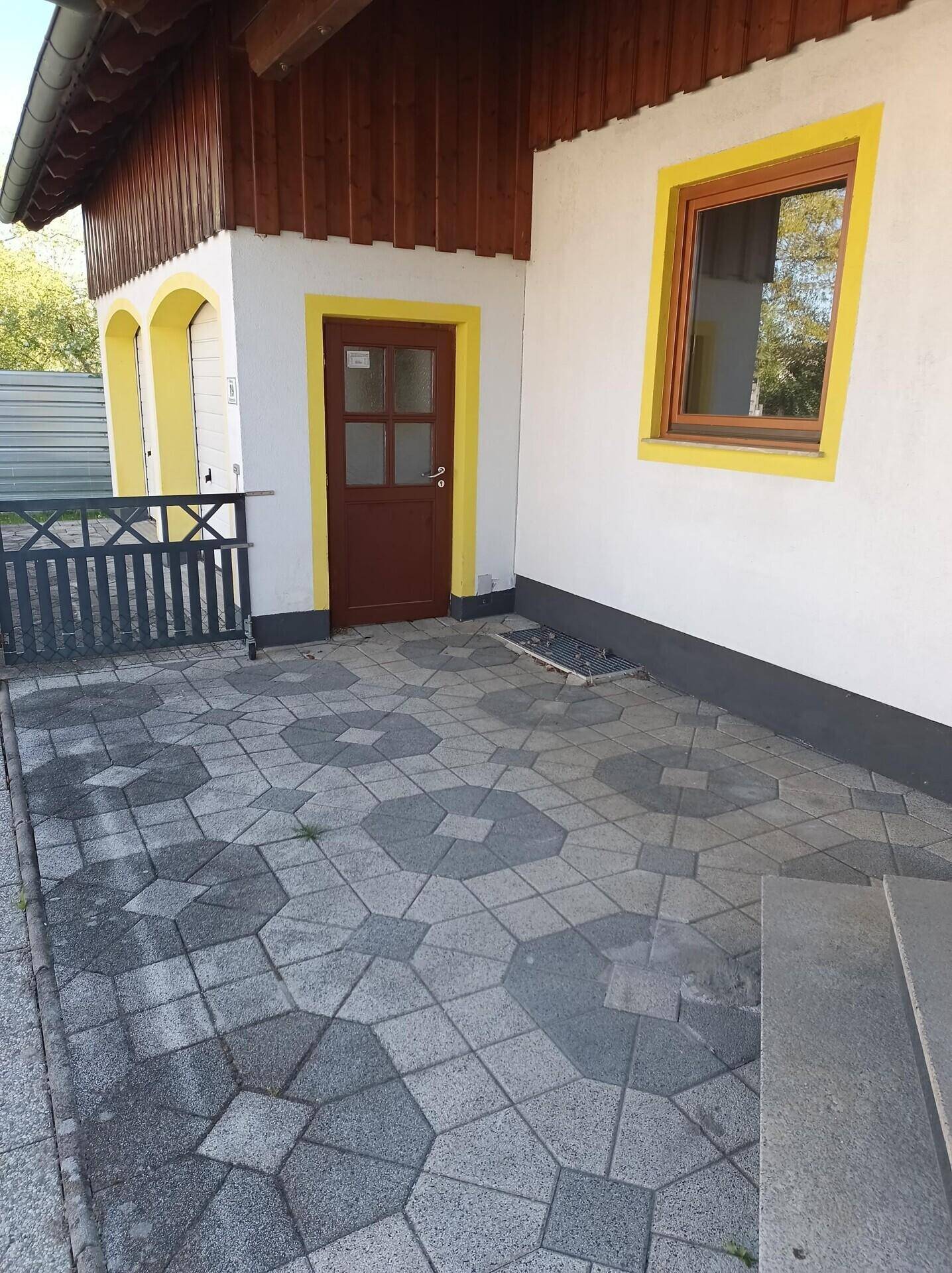 Gepflasterter Eingangsbereich mit kleiner Terrasse und Holzzaun vor der Haustür.