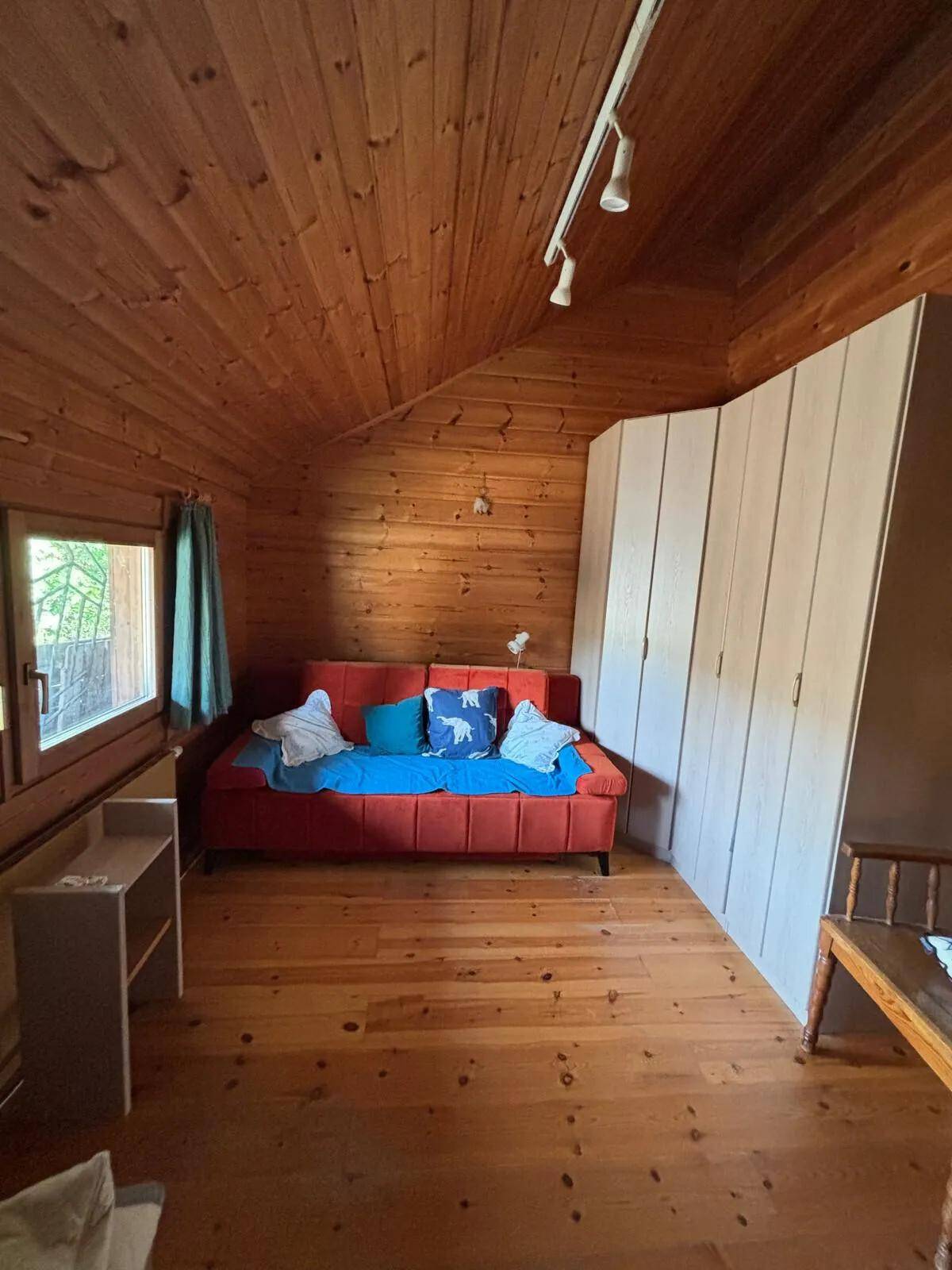 Schlafzimmer mit Holzboden, Dachschräge und einem roten Schlafsofa, umgeben von Holzvertäfelung.