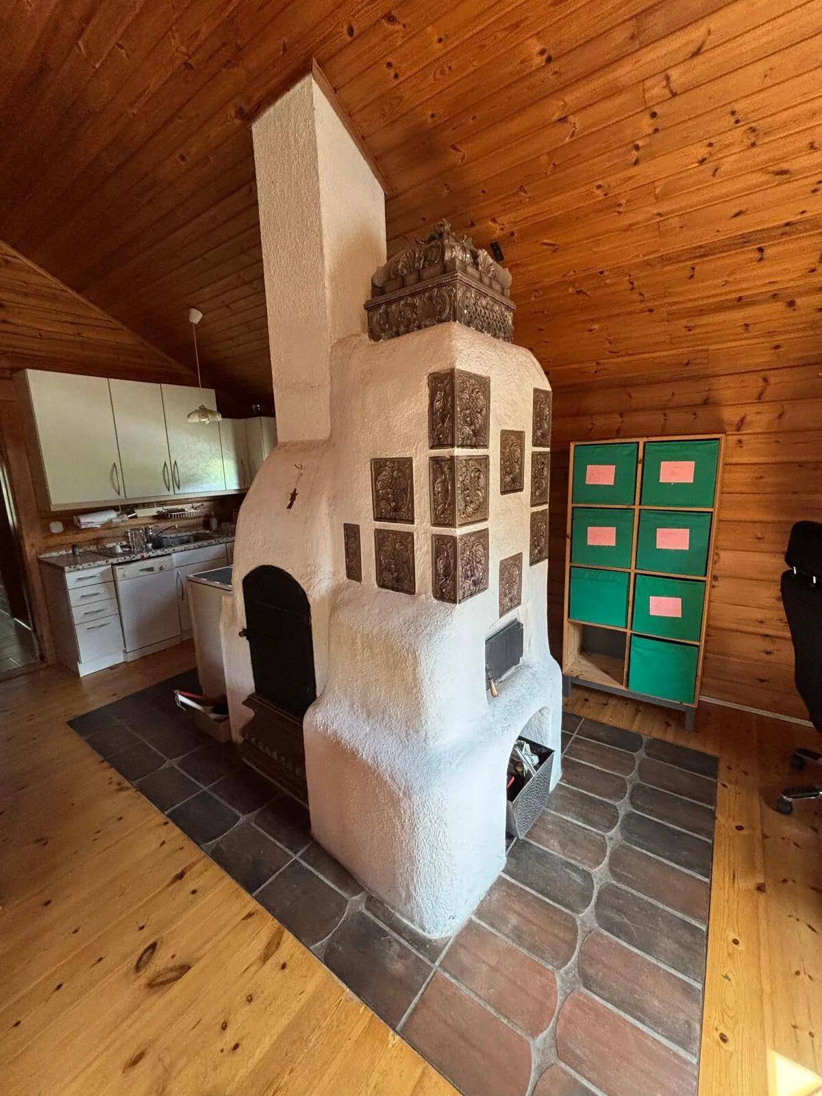 Detailansicht eines traditionellen Kachelofens mit verzierten Fliesen in einem holzgetäfelten Raum.